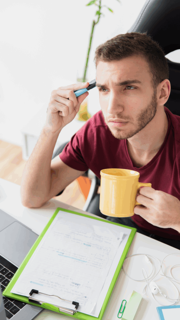 Hombre joven frente a una laptop con expresión pensativa, buscando trabajo y planificando nuevas estrategias.