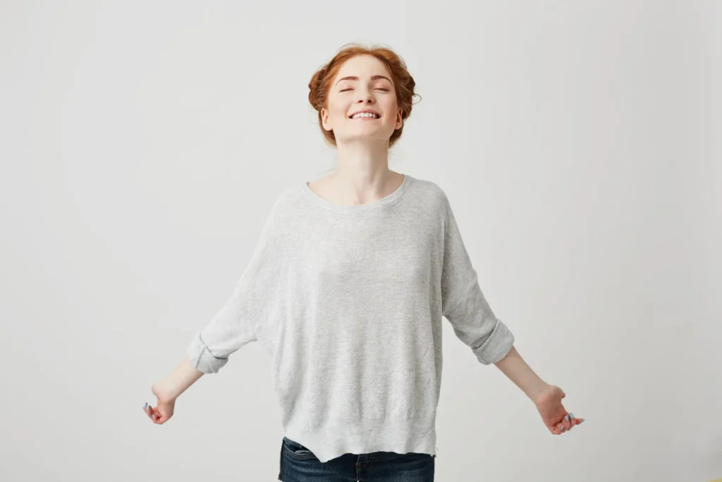 Mujer de pie, sonriendo con los ojos cerrados y las palmas hacia adelante, transmitiendo serenidad durante un proceso de selección.