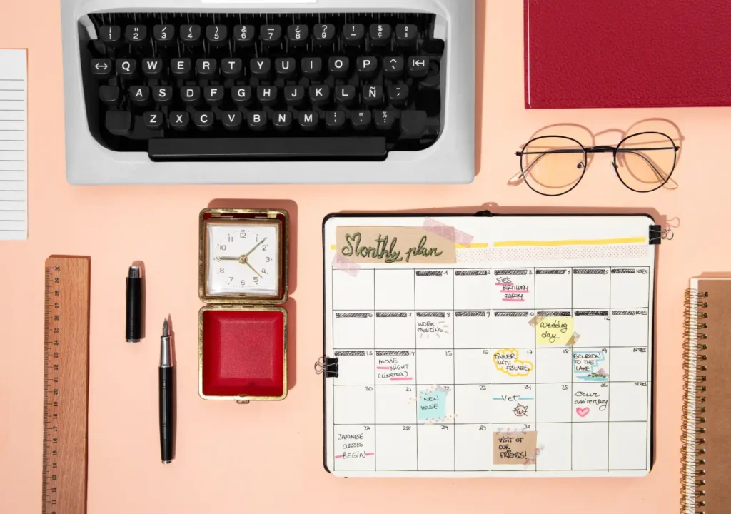 Vista superior de un calendario mensual junto a una máquina de escribir, reloj y gafas, simbolizando la planificación y adaptación en la vida profesional después de los 50