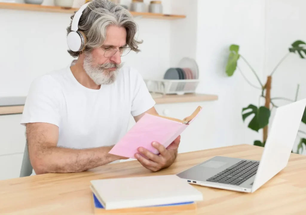 Hombre adulto con auriculares estudiando con un cuaderno y una laptop, representando el reskilling y upskilling en la era digital.