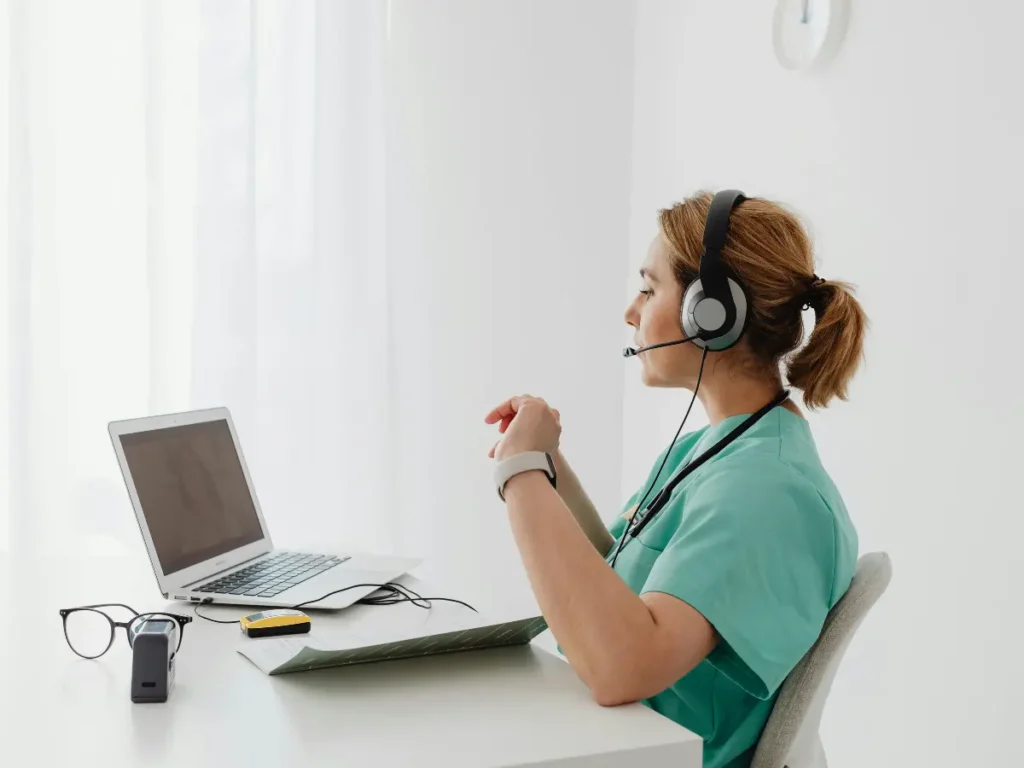Profesional sanitaria utilizando un ordenador portátil y auriculares, representando la transición de la sanidad hacia la tecnología